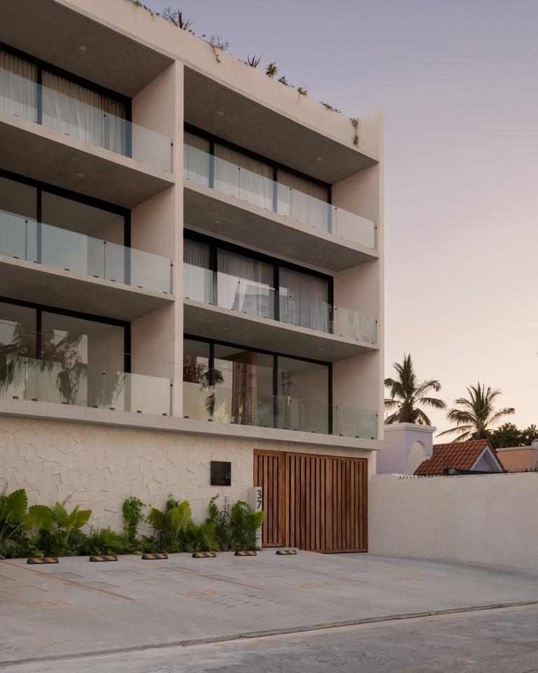 Modern four-story residential building with concrete balconies, white walls, and wooden garage gate at dusk with palm trees visible