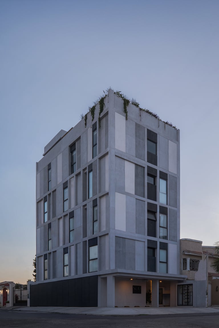 Modern white residential building with glass windows, dark base level, and geometric facade against clear blue sky
